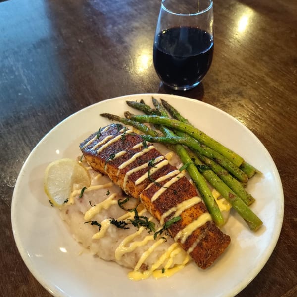 Blackened salmon with mashed potatoes, asparagus, lemon, and a glass of red wine.
