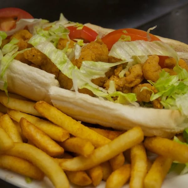 A Sommer's Place fried shrimp po'boy with lettuce and tomato, served with a side of french fries.