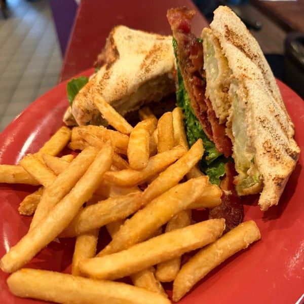 A fried green tomato BLT sandwich with crispy bacon and lettuce, served with golden french fries.