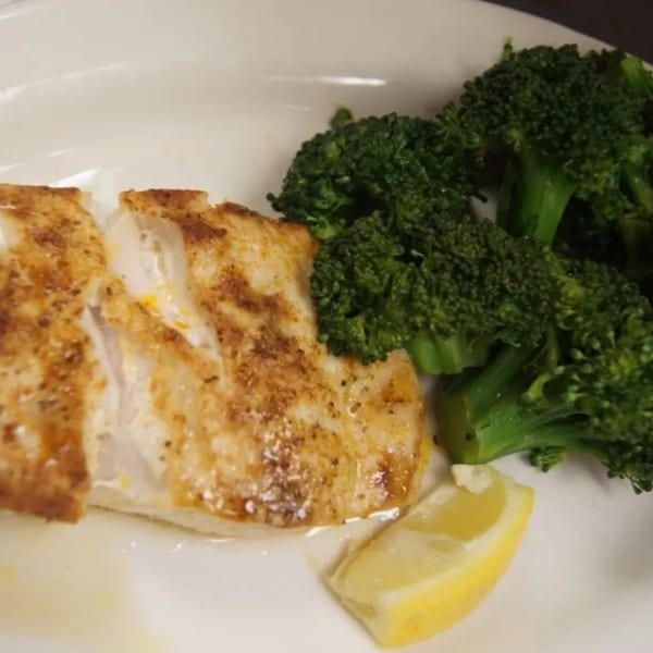 Pan-seared fish fillet with broccoli and a lemon wedge on a white plate at Sommer's Place.