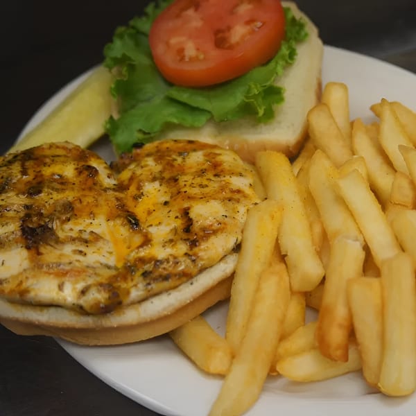 Grilled chicken sandwich with lettuce, tomato, and a side of golden french fries and a pickle.
