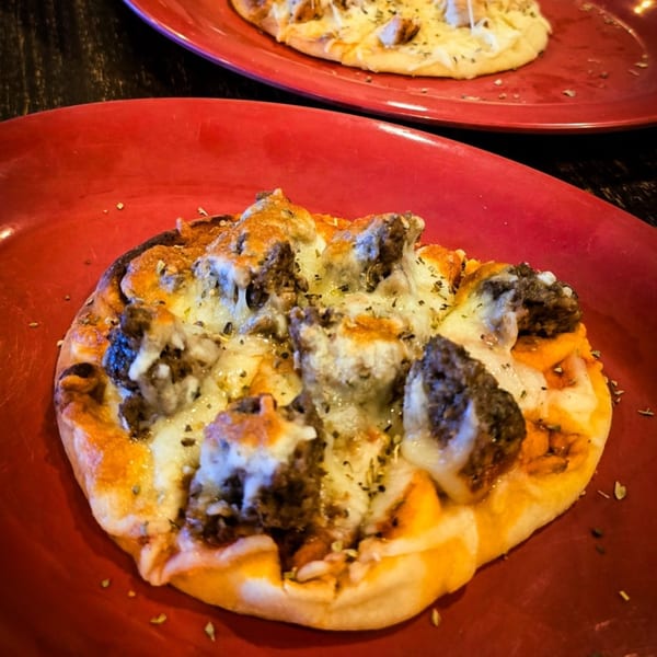 Two mini southern pizzas on red plates, topped with cheese, meat, and herbs.
