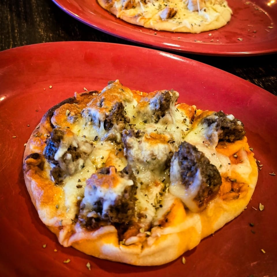 Two mini southern pizzas on red plates, topped with cheese, meat, and herbs.