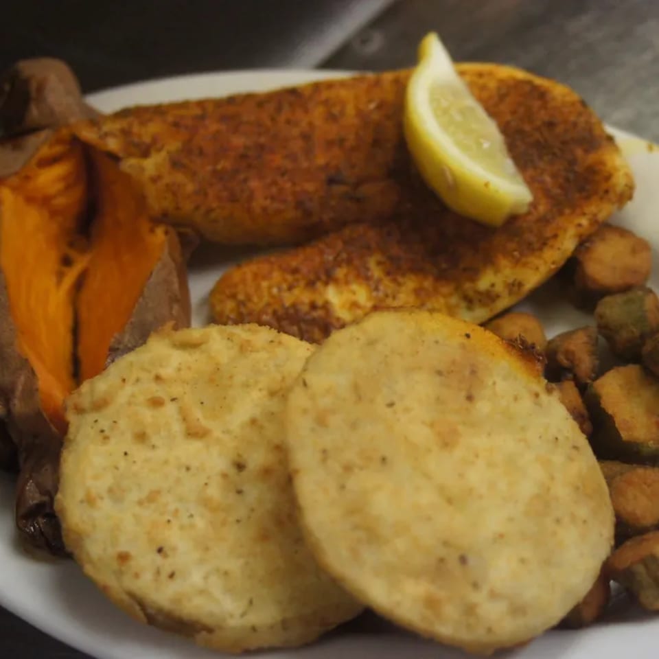 Southern fried fish with a lemon wedge, baked sweet potato, fried green tomatoes, and okra.