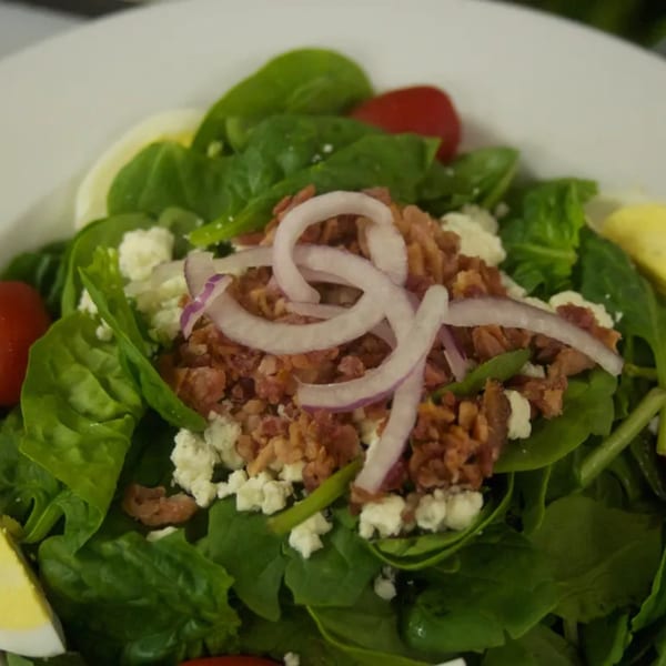 A vibrant spinach salad with crumbled bacon, red onion, feta cheese, cherry tomatoes, and hard-boiled egg.