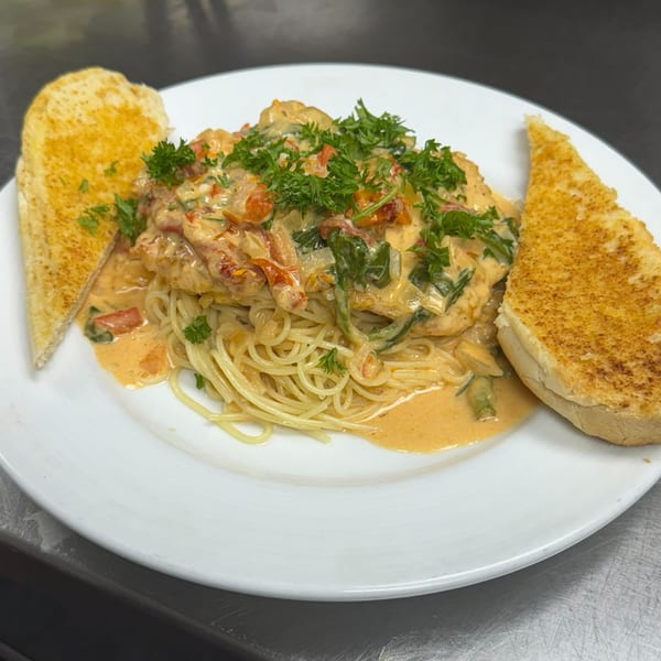 Creamy chicken pasta with sun-dried tomatoes, spinach, and parsley, served with two slices of garlic bread.