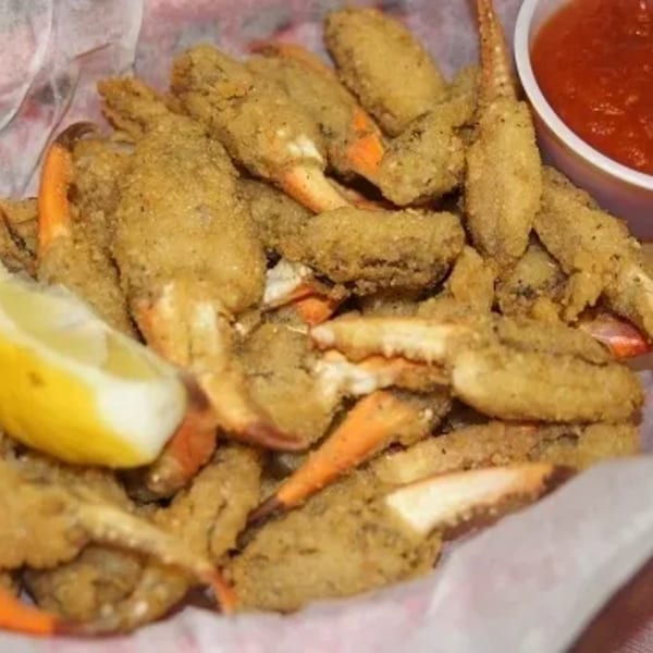 A basket of crispy fried crab claws with a lemon wedge and a side of red dipping sauce.