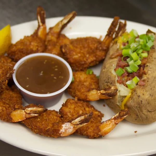 Crispy fried shrimp, a side of dipping sauce, and a loaded baked potato with green onions.