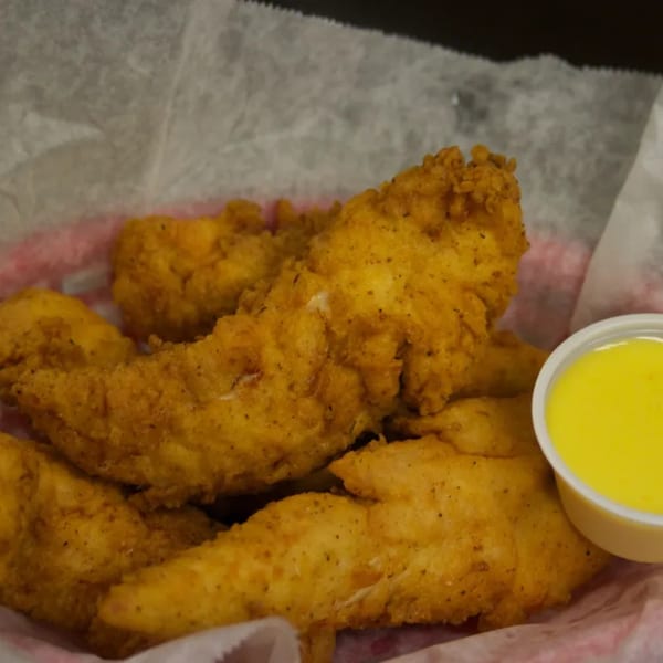 Crispy fried chicken tenders with a side of honey mustard dipping sauce in a red basket.