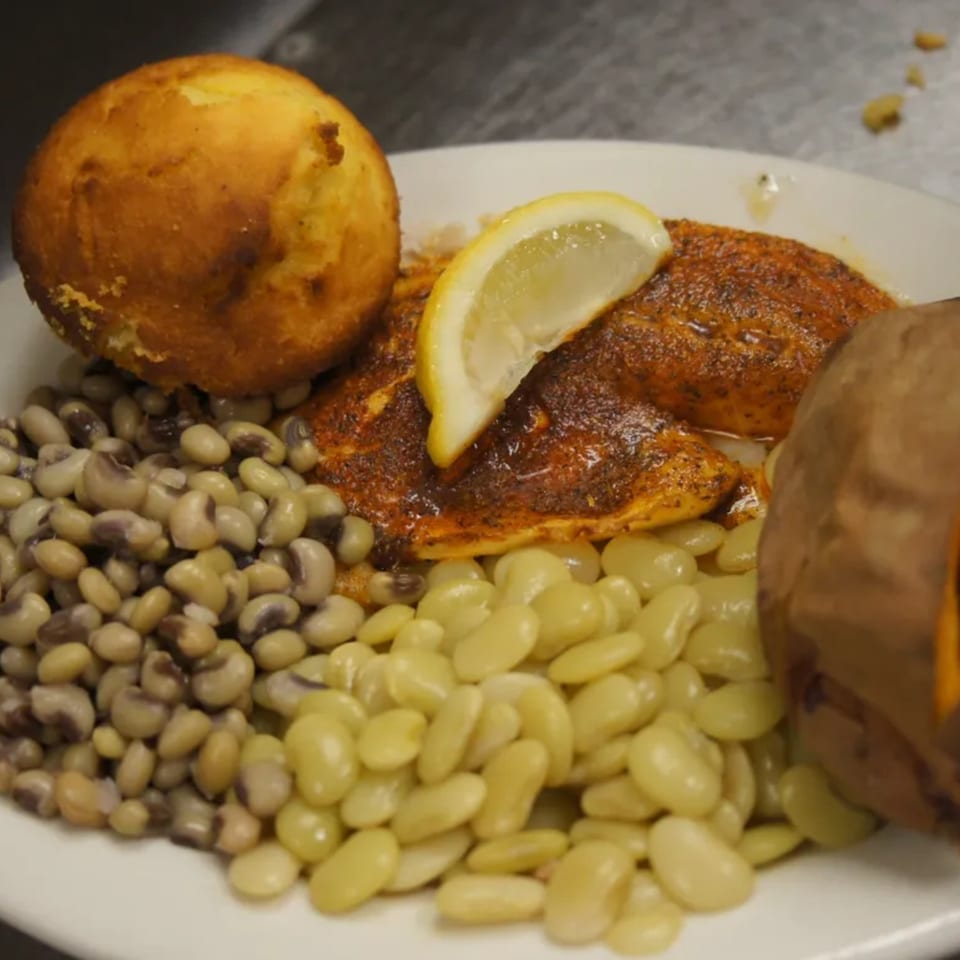 Southern-style plate with blackened fish, cornbread, black-eyed peas, lima beans, and a baked sweet potato.