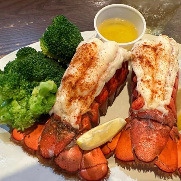 Two lobster tails with drawn butter, lemon, and broccoli on a white plate at Sommer's Place.