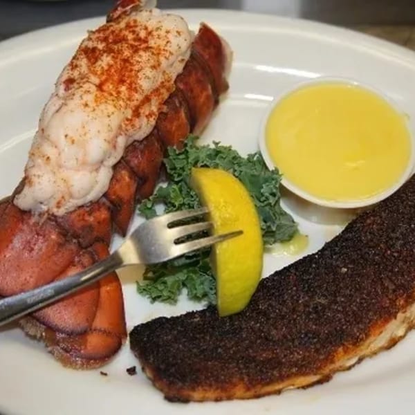 Southern-style lobster tail and blackened fish with lemon, kale, and butter sauce on a white plate.