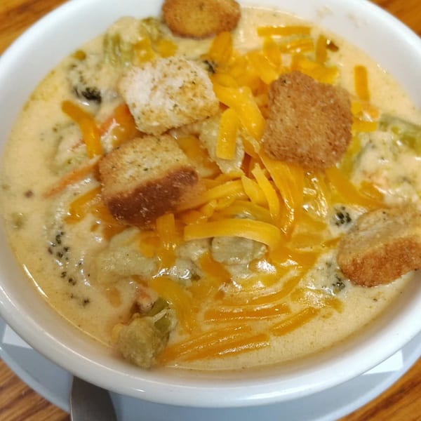 Creamy broccoli cheddar soup with croutons and shredded cheese in a white bowl.