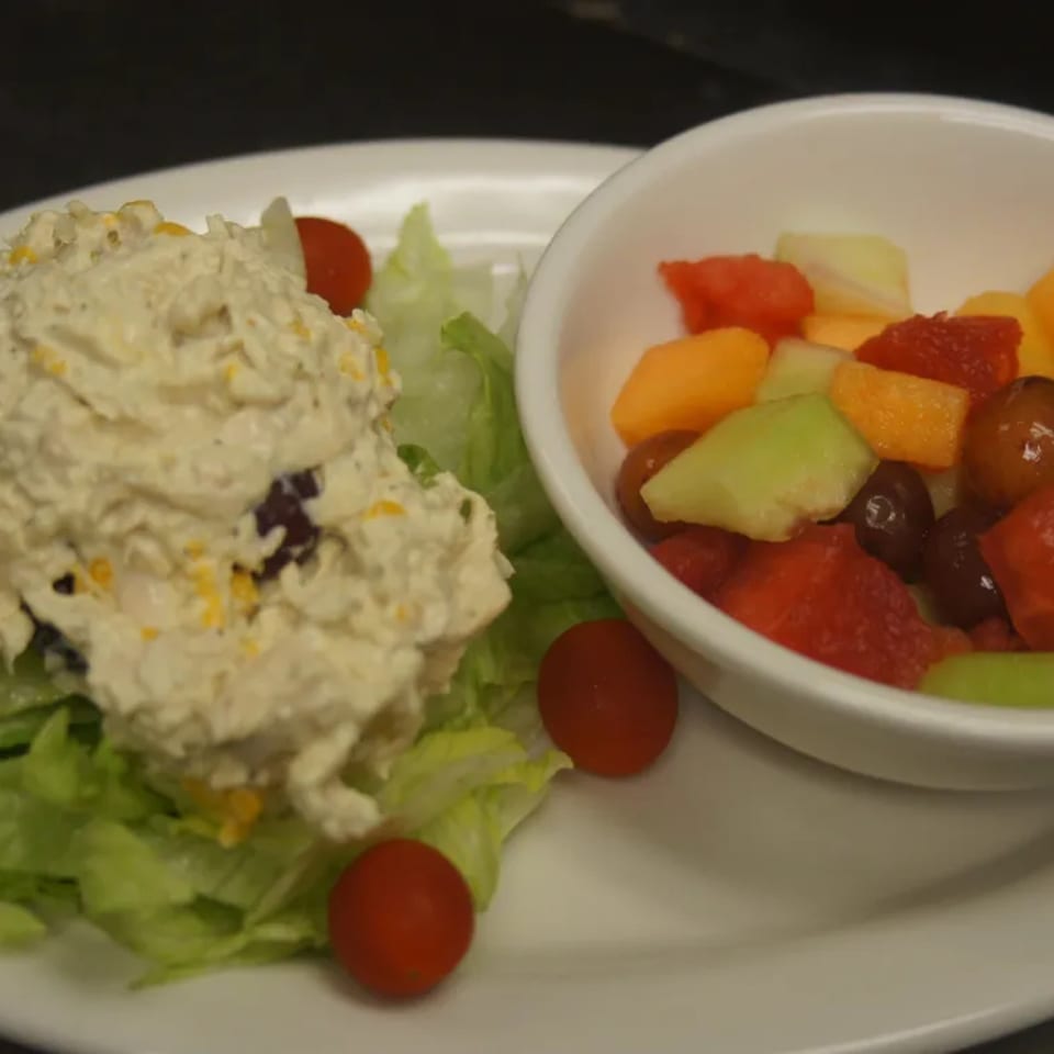 Chicken salad with lettuce and cherry tomatoes, served with a side of fresh fruit.